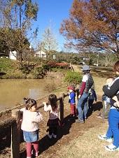 池の周囲の柵に小さな子供たちがつかまり、母親と一緒に池を見ている写真