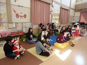 サンタの衣装を着た子供やお母さんの膝の上に座りクリスマス会を楽しむ親子の写真