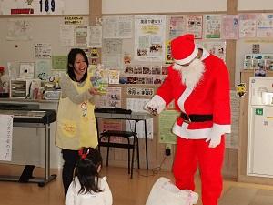 先生がサンタさんへおねだりするように手を出し、サンタの前には女の子が立っている写真