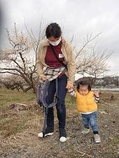 細いあぜ道を、母親が子どもの顔を見ながら手を繋いで歩いている写真