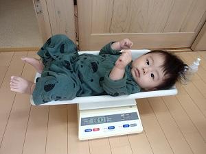 手を握りしめて体重計に寝ころんでいる赤ちゃんの写真