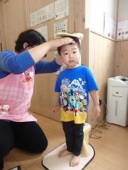 保健師さんに頭を触られながら身長を計っている男の子の写真