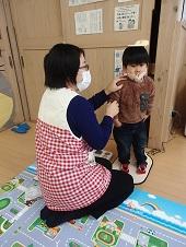 保健師さんが立って身長測定をしている子供の右腕を握っている写真