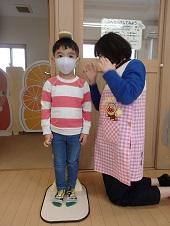 マスク姿の男の子が直立して保健師さんに身長を測定してもらっている写真
