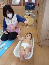 おむつ姿で体重計に乗せられている赤ちゃんの真上でおもちゃを見せている保健師さんの写真