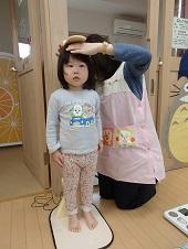 保健師さんが身長計の測る部分を頭の位置にのせ真面目な顔で測定している女の子の写真
