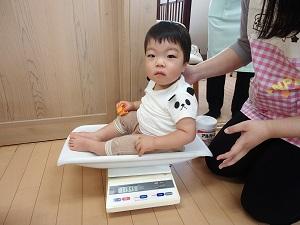 洋服を着た男の子が体重計に座り体重測定している写真