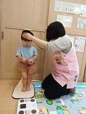 幼児の頭を押さえ、立たせて身長測定をしている保健師さんの写真