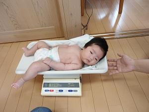 おむつ姿で体重をはかっている眠たそうな赤ちゃんの写真