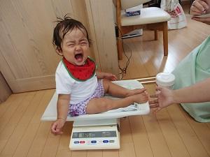 大泣きしながら体重計に座っている赤ちゃんの写真