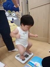 がにまたで頑張って体重計に立っている赤ちゃんの写真