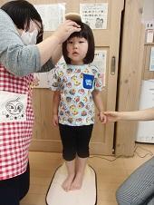 小さな女の子が片手を握られて立って身長測定をしている写真