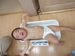 体重計の上に寝て重さを計っている赤ちゃんの写真