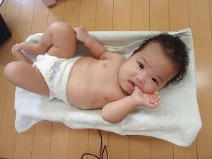 体重計の上に寝て親指をくわえている赤ちゃんの写真