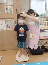 身長を計っている男の子とメモリを読んでいる保健師の写真