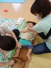身長計に寝ている赤ちゃんの頭を両手で支えている母親とメモリを読んでいる保健師の写真