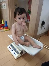 体重計の上に座って重さを計っている赤ちゃんの写真