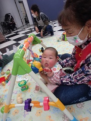 保育ボランティアのお膝でお座りしながら遊ぶ乳児