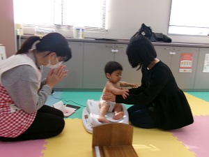 体重を測り終えママのところに戻る幼児と拍手をする助産師