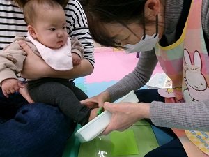 足型をとる先生と、見つめる赤ちゃん