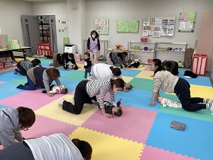 赤ちゃんを仰向けに寝かせ、向き合うように四つ這いになり、いないいないばあを楽しむ親子たち