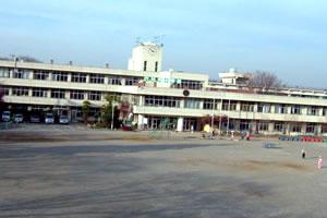 学校のグラウンドの奥に白い壁の3階建て校舎が写っている写真