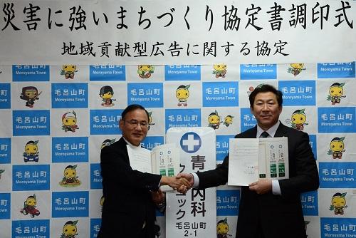 災害に強いまちづくり協定書調印式で関係者2名が協定書をみせながら握手をしている写真