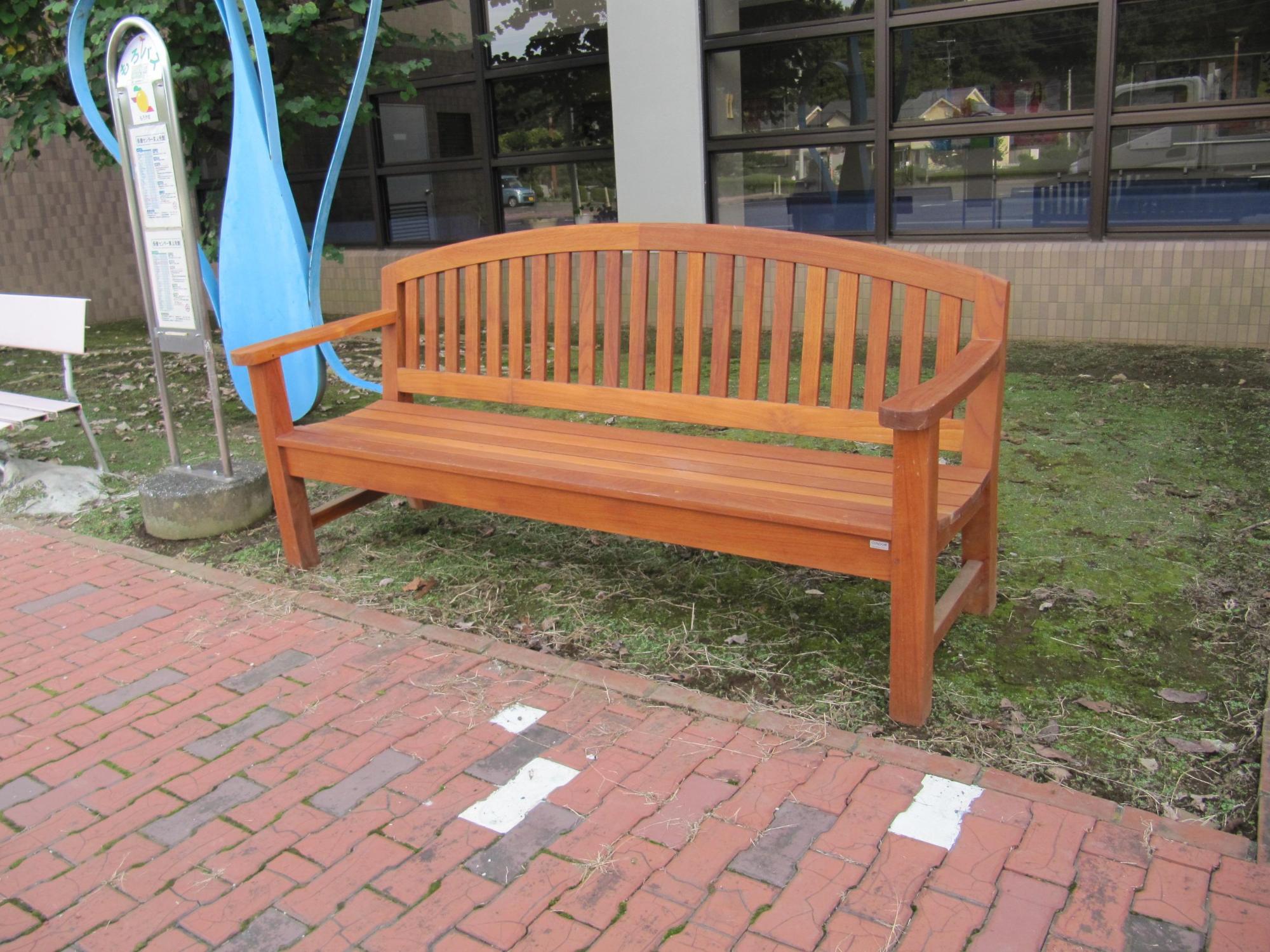 肘掛け付きの木製のベンチが保健センター東公民館1のバス停に設置されている写真
