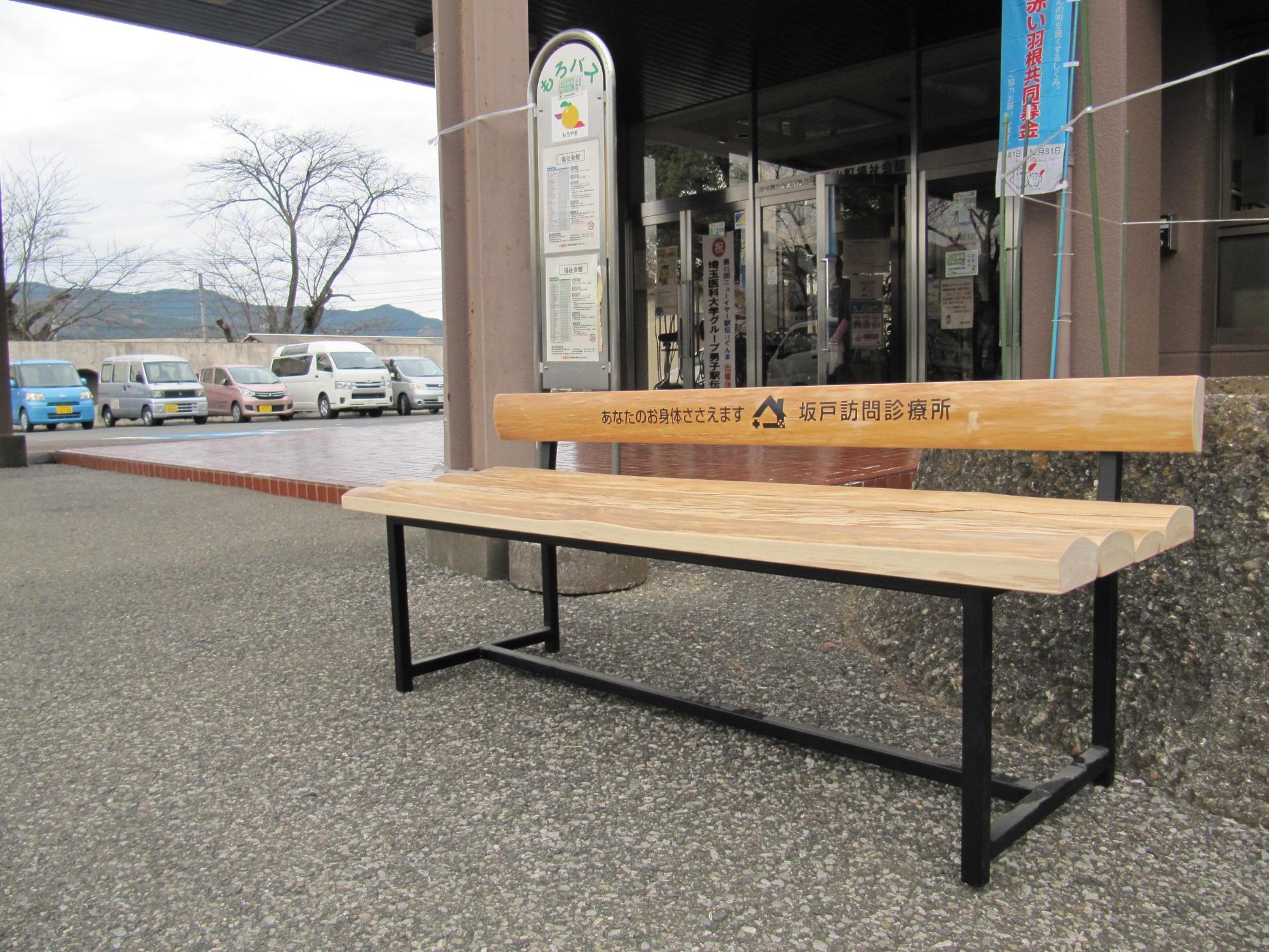 木製のベンチの背もたれに「坂戸訪問診療所」と文字の入ったベンチが福祉会館前のバス停に設置されている写真